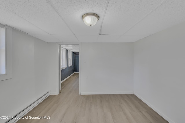 spare room featuring a paneled ceiling, light wood-type flooring, and baseboard heating