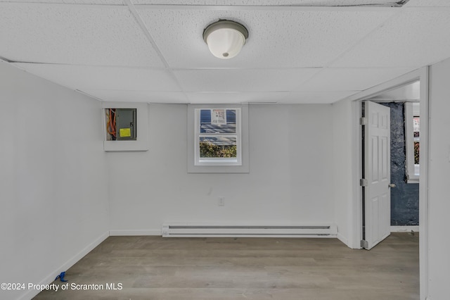 basement featuring light wood-type flooring, a paneled ceiling, and a baseboard radiator