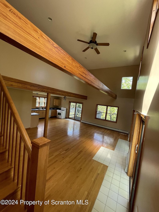 unfurnished living room with ceiling fan, a towering ceiling, baseboard heating, and light tile patterned floors