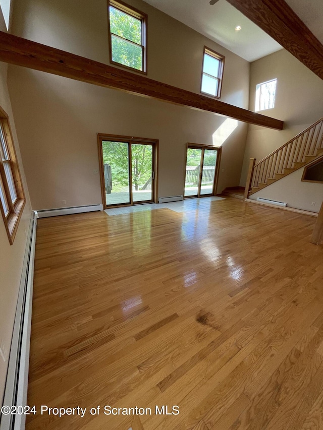 unfurnished living room with light hardwood / wood-style floors, a towering ceiling, and a baseboard radiator