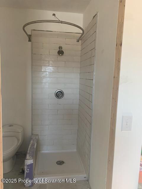 bathroom with a tile shower and toilet