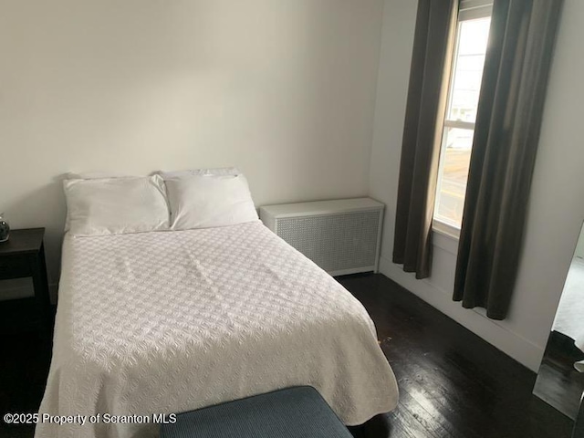 bedroom with dark hardwood / wood-style flooring and radiator