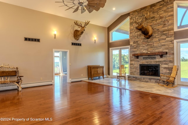 unfurnished living room with ceiling fan, baseboard heating, hardwood / wood-style flooring, high vaulted ceiling, and a stone fireplace