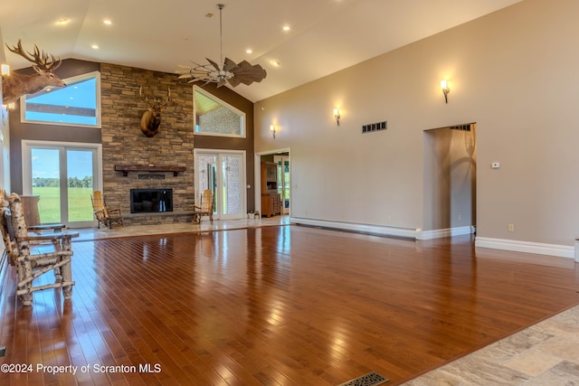 living room featuring ceiling fan, a high ceiling, a stone fireplace, a baseboard heating unit, and wood-type flooring