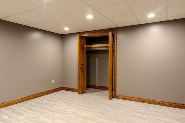 unfurnished bedroom with a paneled ceiling, a closet, and light hardwood / wood-style flooring