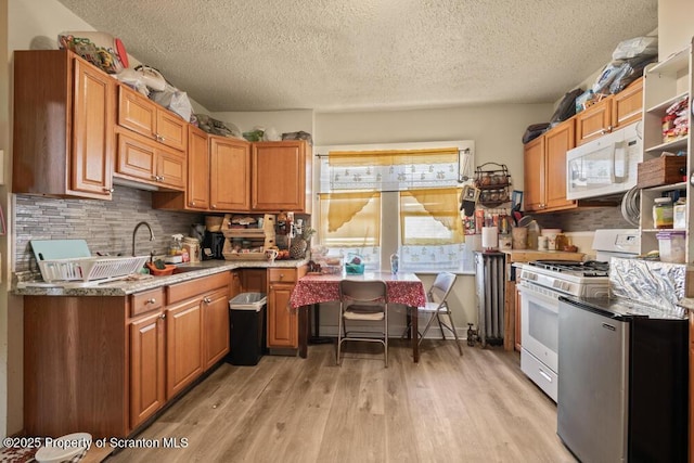 kitchen with white appliances, brown cabinetry, light wood-style flooring, a sink, and decorative backsplash