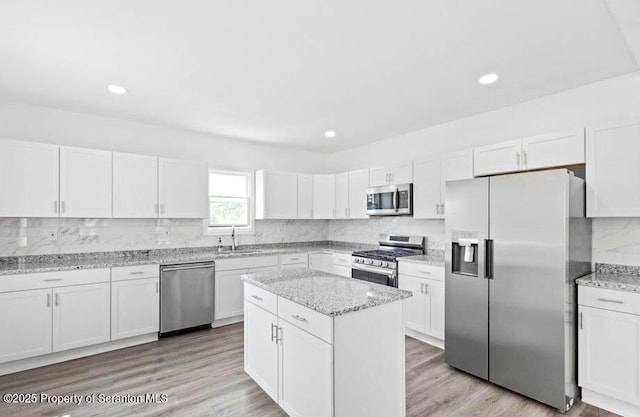 kitchen featuring sink, light stone counters, white cabinets, stainless steel appliances, and backsplash