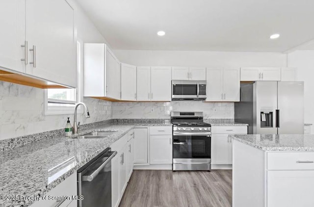 kitchen with appliances with stainless steel finishes, tasteful backsplash, sink, white cabinets, and light stone countertops