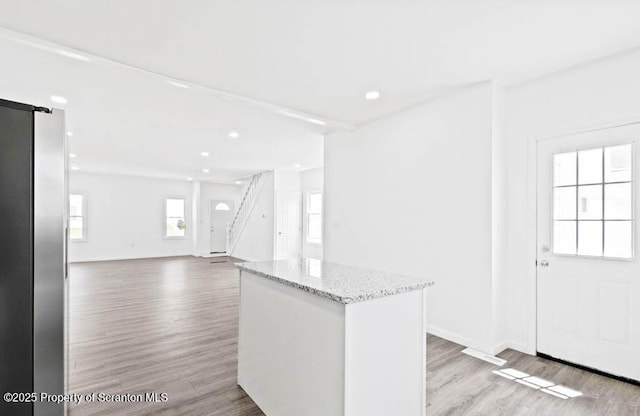 kitchen featuring light hardwood / wood-style flooring, white cabinetry, a center island, light stone countertops, and a barn door