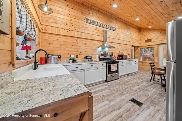 kitchen with wall chimney exhaust hood, wood walls, white cabinetry, and appliances with stainless steel finishes