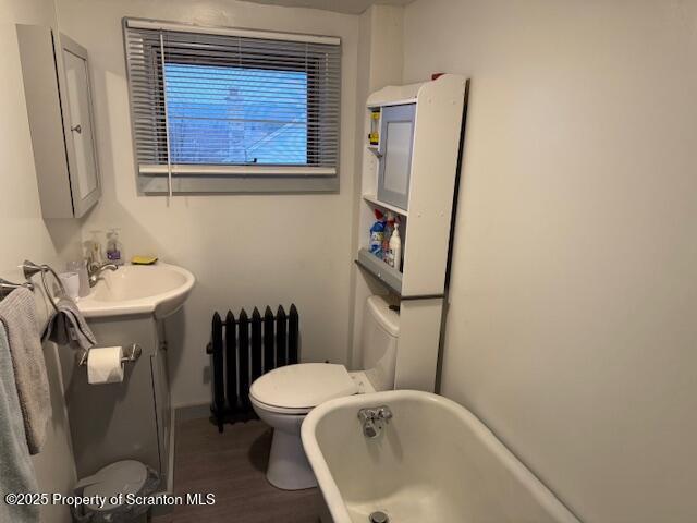 bathroom featuring radiator, vanity, a tub to relax in, toilet, and hardwood / wood-style flooring