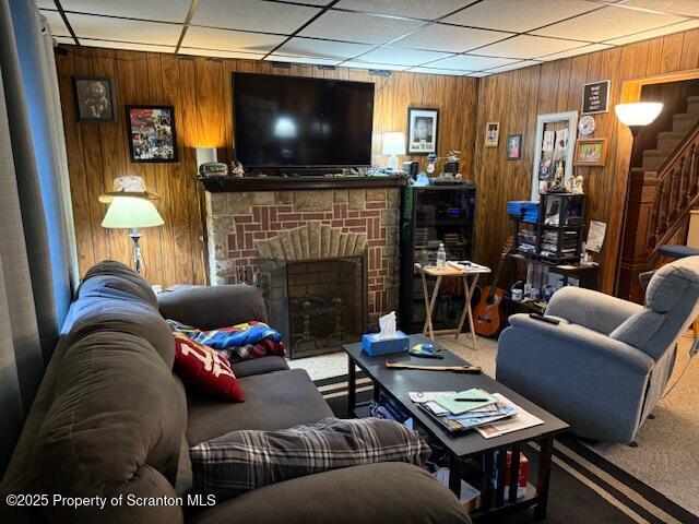 living room with carpet, a stone fireplace, and wooden walls