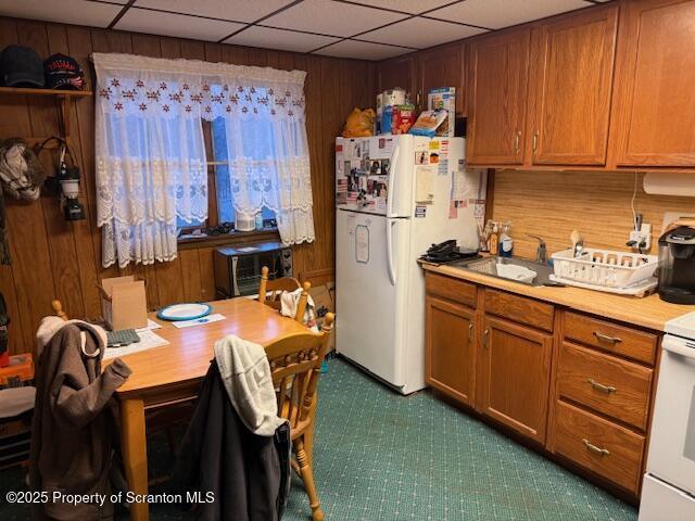 kitchen with white fridge, range, wooden walls, and sink