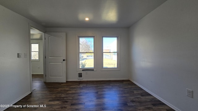 empty room with heating unit, dark wood-style floors, and baseboards