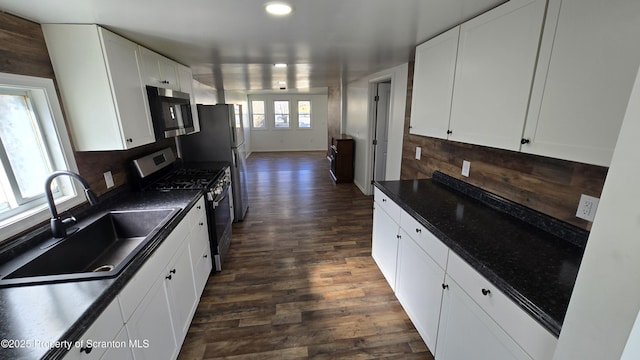 kitchen featuring dark wood-style flooring, a sink, appliances with stainless steel finishes, dark countertops, and tasteful backsplash