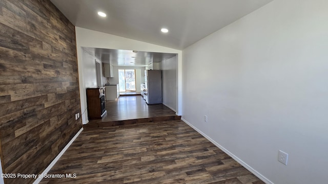 corridor featuring wooden walls, dark wood-type flooring, baseboards, vaulted ceiling, and recessed lighting