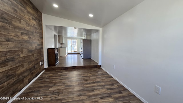 hall featuring wooden walls, baseboards, lofted ceiling, recessed lighting, and dark wood-style flooring