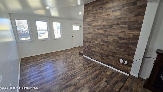 spare room featuring lofted ceiling, recessed lighting, wood walls, baseboards, and dark wood-style flooring