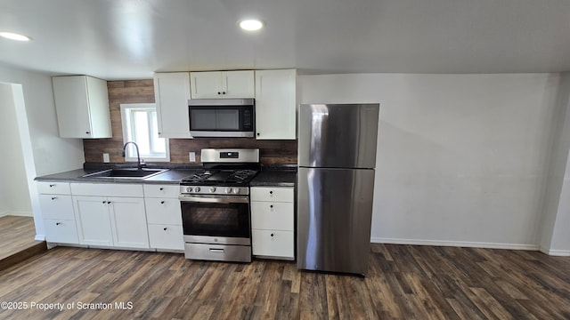 kitchen featuring dark countertops, dark wood finished floors, stainless steel appliances, white cabinetry, and a sink