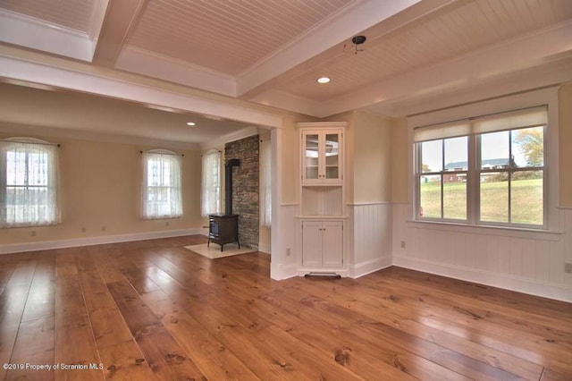 unfurnished living room with beam ceiling, wood-type flooring, a wood stove, and crown molding