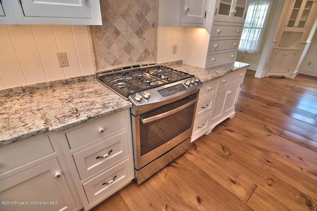 kitchen featuring white cabinetry, light stone counters, backsplash, light hardwood / wood-style floors, and stainless steel range with gas stovetop