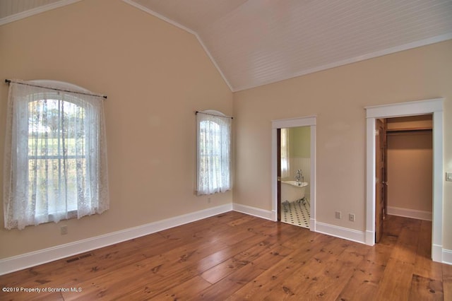 unfurnished bedroom featuring ensuite bathroom, a walk in closet, vaulted ceiling, light wood-type flooring, and a closet