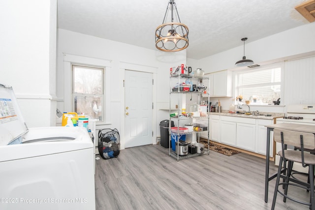 kitchen featuring white cabinetry, sink, light hardwood / wood-style floors, and hanging light fixtures