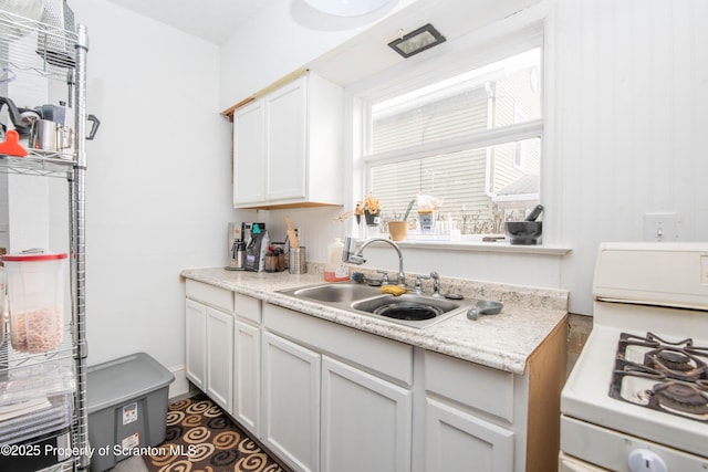 kitchen with light stone countertops, sink, white cabinets, and white gas range oven