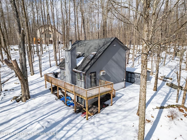 snow covered rear of property featuring a shingled roof, a chimney, and a wooden deck