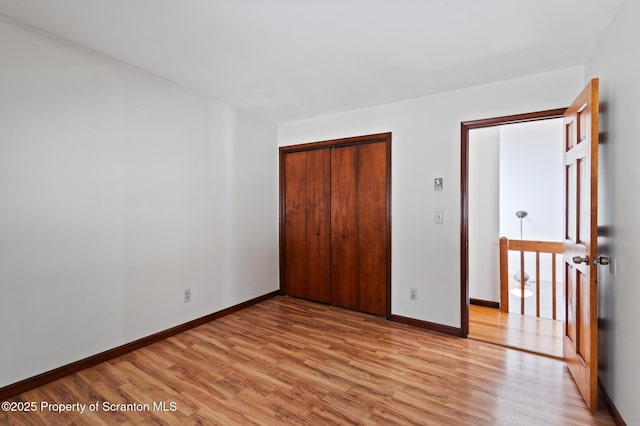 unfurnished bedroom featuring light wood-type flooring, baseboards, and a closet