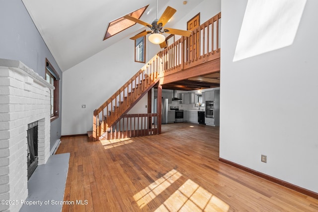 unfurnished living room with ceiling fan, stairway, wood finished floors, a fireplace, and high vaulted ceiling