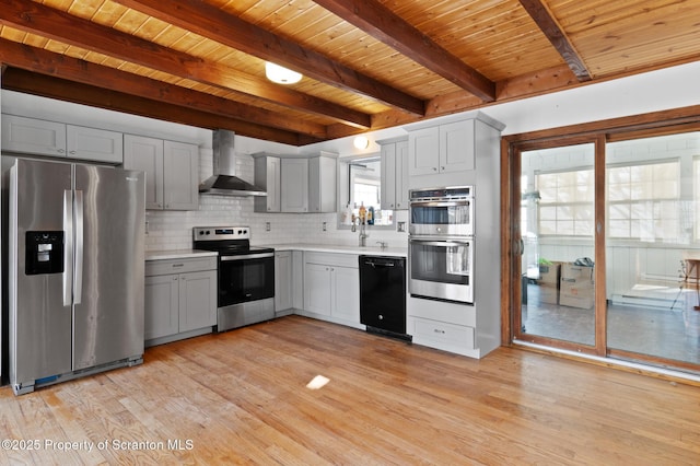 kitchen featuring light countertops, backsplash, appliances with stainless steel finishes, light wood-style floors, and wall chimney range hood