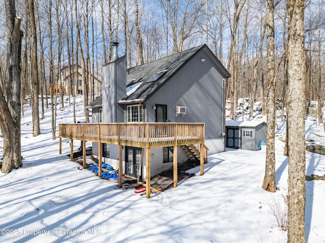 snow covered rear of property with a chimney, a storage unit, an outdoor structure, a wooden deck, and stairs