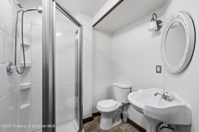 bathroom with toilet, a shower stall, baseboards, and a sink