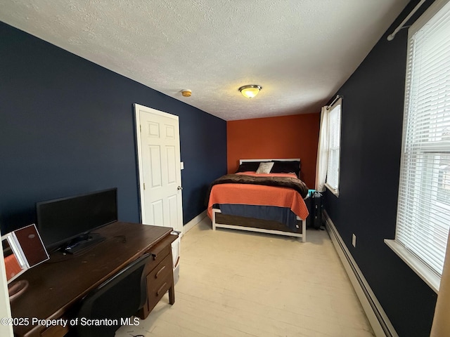 bedroom featuring multiple windows, a textured ceiling, and a baseboard heating unit