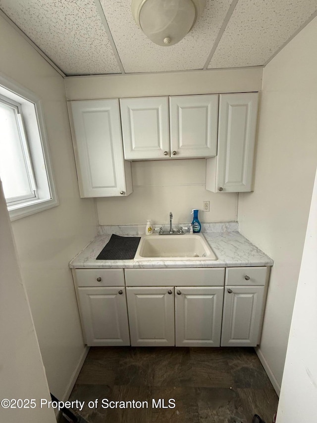 kitchen featuring a paneled ceiling, sink, and white cabinets