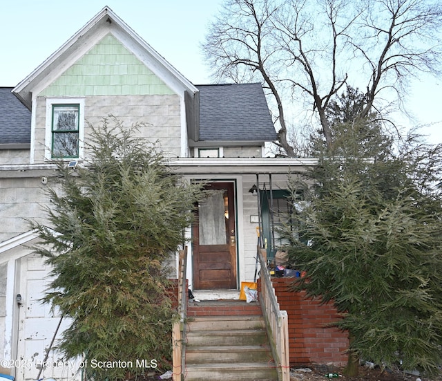 view of front facade with entry steps, a shingled roof, and brick siding