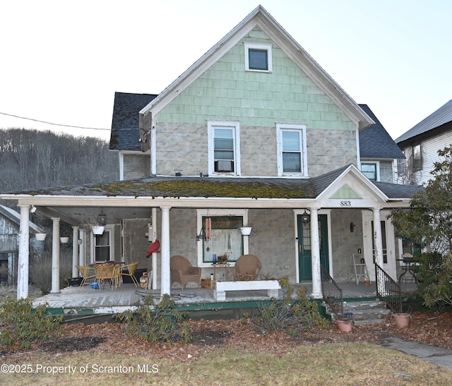 view of front of house featuring covered porch, a shingled roof, and stone siding