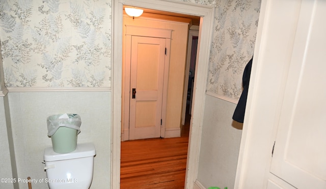 bathroom with wood finished floors, a wainscoted wall, toilet, and wallpapered walls