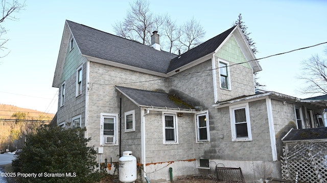 rear view of property featuring roof with shingles, a chimney, and cooling unit