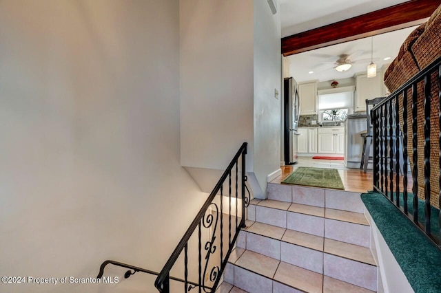 staircase featuring tile patterned floors, ceiling fan, and beamed ceiling