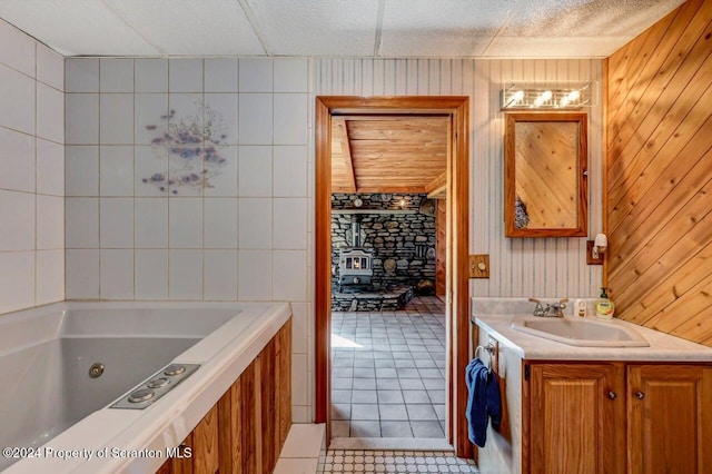 bathroom with a washtub, tile patterned floors, a paneled ceiling, wooden walls, and vanity