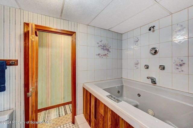 bathroom with tile patterned flooring, a drop ceiling, and a tub to relax in