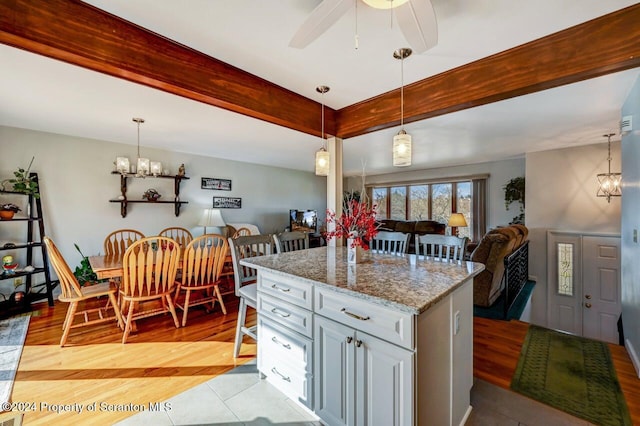 kitchen featuring ceiling fan, light stone counters, light hardwood / wood-style floors, decorative light fixtures, and a kitchen island