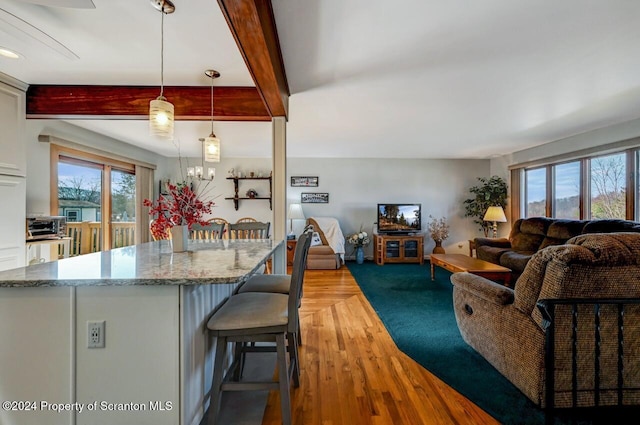 kitchen with beam ceiling, light stone counters, pendant lighting, a kitchen bar, and white cabinets