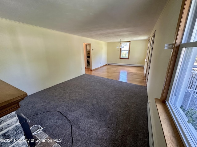 unfurnished living room featuring carpet flooring, a chandelier, and a baseboard heating unit