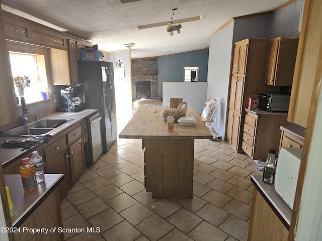 kitchen featuring a center island, a stone fireplace, sink, vaulted ceiling, and a textured ceiling