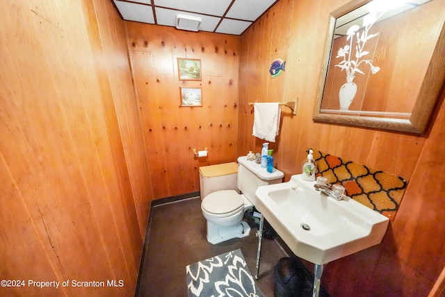 bathroom featuring sink, toilet, a drop ceiling, and wood walls