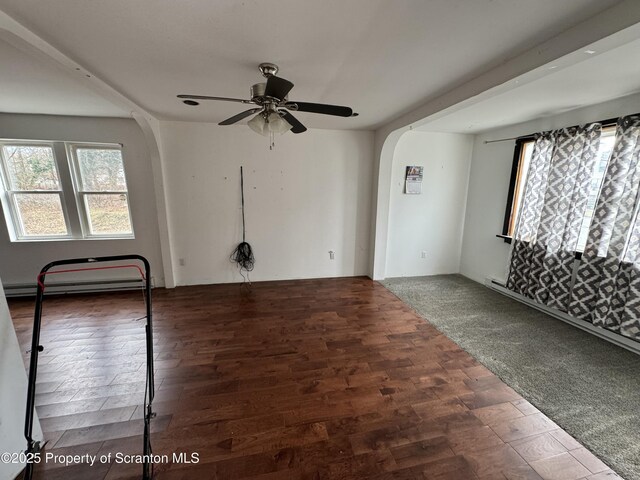 unfurnished room with arched walkways, a baseboard heating unit, ceiling fan, and wood finished floors