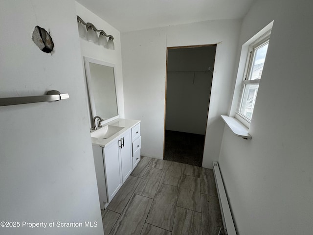 bathroom featuring a baseboard heating unit, a walk in closet, and vanity